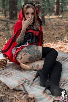 a woman sitting on top of a blanket in the woods with her hands up to her mouth