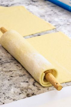 rolled up dough sitting on top of a counter next to a rolling pin with a wooden handle