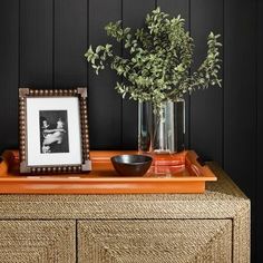 an orange dresser topped with a vase filled with flowers and a black wall behind it