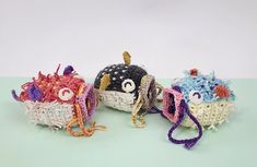 three small crocheted items are sitting on a table together, one has an eyeball and the other is a monster