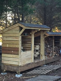 a small wooden building with logs stacked on the ground next to it and trees in the background