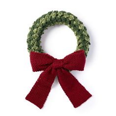 a green and red knitted wreath with a bow on the front, sitting against a white background