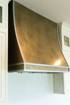 a gold hood in the corner of a kitchen with white cabinets and cupboards behind it