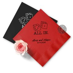 two red and black paper napkins with dice on them next to a pink rose