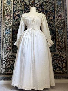 The perfect base to any historically inspired outfit, our 100% cotton smocked chemise dress is sure to please! This stunning gown is made of floral embroidered cotton, and trimmed with floral cotton lace. It features smocked shirring all the way around the bodice, drawstrings for size adjustment, bishop sleeves, etc. White 18th Century Dress, Chemise Ideas, White Cotton Regency Prairie Dress, White Cotton Regency Style Prairie Dress, Elegant White Cotton Prairie Dress, Cotton Victorian Cottagecore Dress For Daywear, Cotton Victorian Dress With Long Sleeves In Regency Style, Cotton Victorian Dress With Long Sleeves In Cottagecore Style, Cotton Long Sleeve Victorian Cottagecore Dress