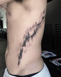 a man's lower back with trees and mountains tattoo on his left side ribcage