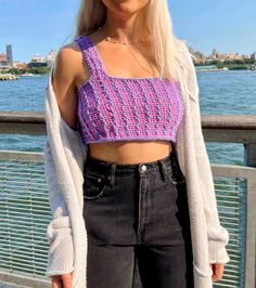 a woman with blonde hair wearing a purple knitted crop top and black denim shorts