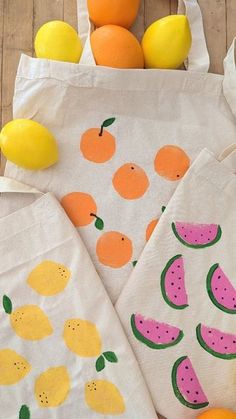 three bags with fruit painted on them sitting next to some lemons and oranges