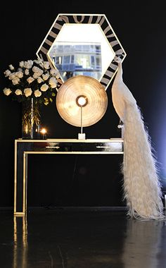 a white peacock standing on top of a table next to a mirror and vase with flowers