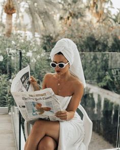 a woman sitting in a chair reading a newspaper while wearing a towel on her head