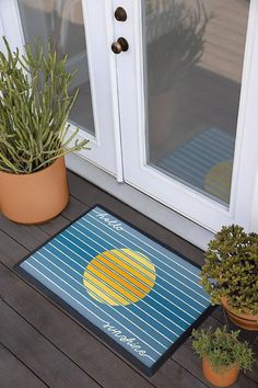 two potted plants sit on the porch next to a door mat that says welcome home