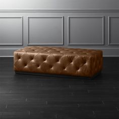 a brown leather bench sitting on top of a hard wood floor next to a wall