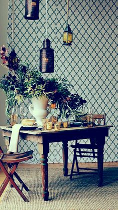 a dining room table with flowers and candles on it next to a wallpapered wall