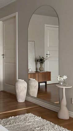 a large mirror sitting on top of a wooden floor next to a white vase filled with flowers