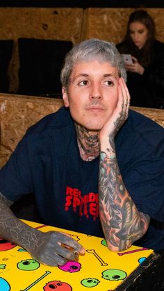 a man sitting at a table with tattoos on his arm and hand next to him