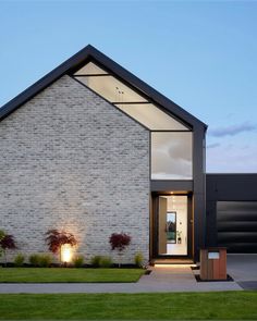 a modern house with an open front door and white brick facade at dusk, lit up by lights on the windows