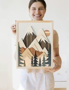 a woman holding up a wooden cutout with mountains and trees in the woods on it