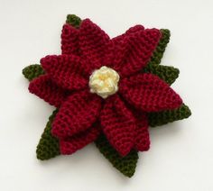 a crocheted red poinsettia with green leaves and a white flower