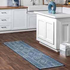 a kitchen with white cabinets and wood flooring on the wooden floor, along with a blue runner rug