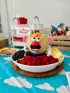 a bowl of fruit with a clown face on it and other food items in the background