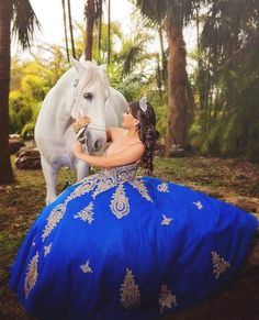 a woman in a blue dress sitting next to a white horse