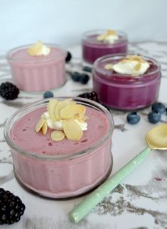 three desserts in small bowls on a table with berries and blueberries around them