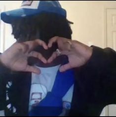 a man making a heart shape with his hands while wearing a hat and holding something in front of his face