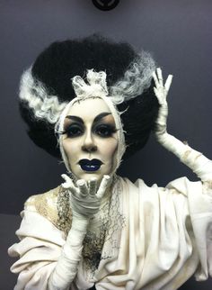 a woman with black hair and white make - up is posing for the camera while wearing an elaborate wig