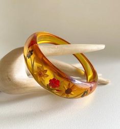 Gorgeous & becoming rare,  Art Deco 1930s reverse carved bakelite bangle In translucent, apple juice Bakelite which is asymmetrical in shape  Reverse carved to the thicker side with flowers & leaves design  looks lovely when it catches the light , almost glows , quite stunning ! Test Positive for Bakelite  bracelet size : Graduating from 1" (2.4 cm)  at widest part  down to 3/8" (0.8cm)  2 & 1/2 " (6.5cm)  internal diameter  In great vintage condition , very light surface wear commensurate  (very light scratches ) with its age , no cracks or damage & no wear to the reverse colours please note - any white marks in my photos are light reflection   A beatiful item for the collector ! Vintage Amber Bangle Bracelet, Vintage Bakelite Bangle Jewelry, Vintage Bakelite Bangle, Vintage Resin Bracelet, Vintage Lucite Bangle Bracelet, Vintage Amber Resin Jewelry, Vintage Resin Bangle, Vintage Carved Orange Jewelry, Orange Carved Vintage Jewelry