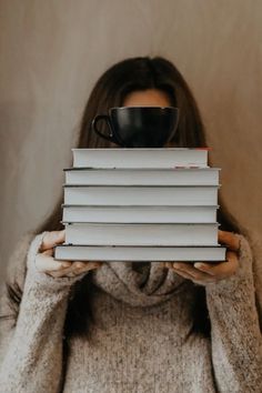 a woman holding a stack of books and a cup of coffee in front of her face