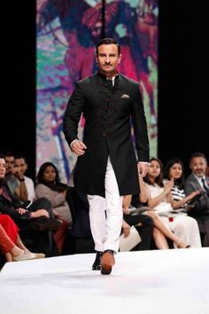 a man is walking down the runway in a black suit and white pants, while people watch