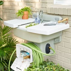 an outdoor sink with plants and gardening tools in the drainer box next to it