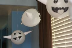 three balloons with faces hanging from them in front of a window, one is white and the other is black