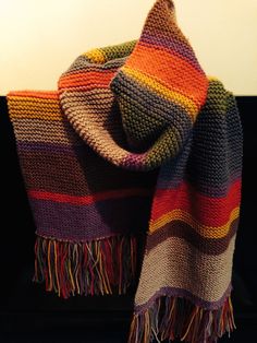 a multicolored knitted blanket sitting on top of a black couch next to a white wall