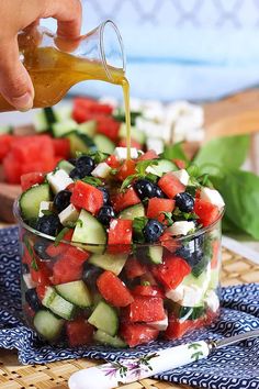 someone is pouring dressing onto a salad in a glass bowl with cucumbers and blueberries