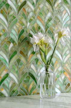 two white flowers in a glass vase on a marble table with green and gold wallpaper