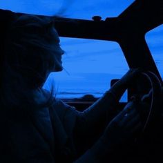 a woman driving a car at night with the lights on and blue sky in the background