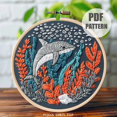 an embroidery pattern with a dolphin in the water surrounded by plants and corals on a wooden table