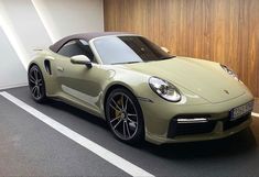 a green sports car parked in a parking lot next to a wooden paneled wall