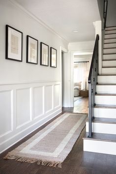 there is a rug on the floor in front of some stairs and framed pictures hanging on the wall