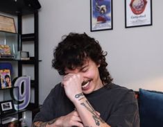 a man with tattoos on his arm sitting in front of a book shelf filled with books