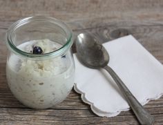 a glass jar filled with oatmeal next to a spoon on top of a wooden table