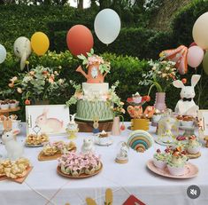 a table topped with lots of cakes and desserts next to balloons in the air