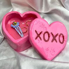 two pink heart shaped boxes sitting on top of a white cloth covered bed with the word xoxo painted on them