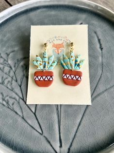 a pair of earrings sitting on top of a piece of paper next to a plant