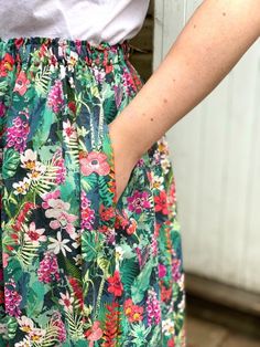 a woman wearing a skirt with flowers and leaves on it, standing in front of a door