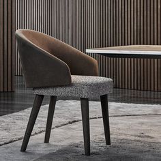 an upholstered chair sits in front of a round table with a wooden paneled wall behind it