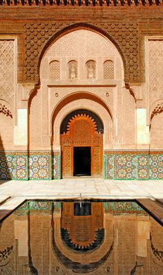 an ornate doorway with tiled walls and floor reflecting in the water at its reflection pool