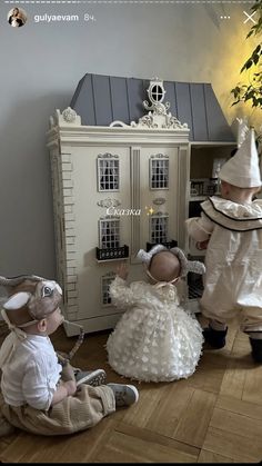 two dolls are sitting on the floor in front of a doll house and another doll is standing up