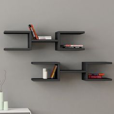 three black shelves with books and vases on them against a gray wall in a room